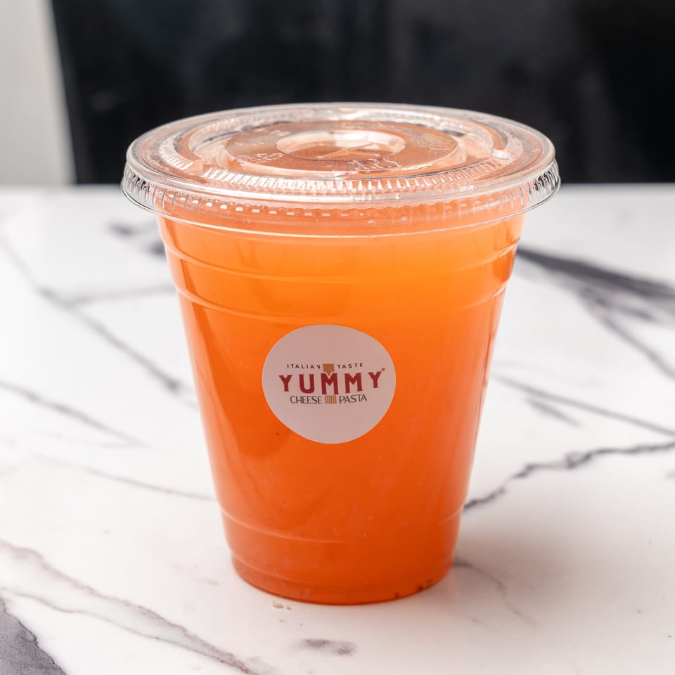 A plastic cup of orange juice with a "Yummy Italian Taste" sticker sits on a marble surface.