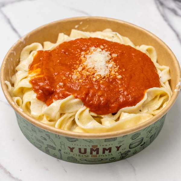 Yummy Cheese Pasta with fettuccine, red sauce, and grated cheese in a branded takeout container.