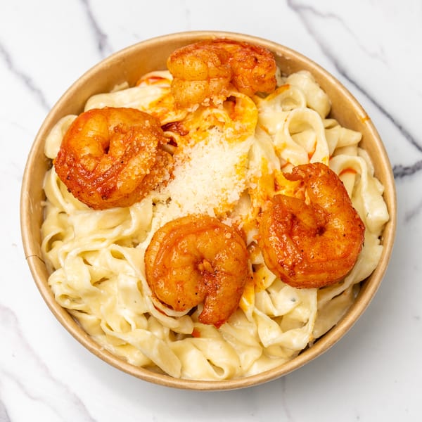 Creamy fettuccine alfredo with five large, seasoned shrimp and grated cheese in a bowl.