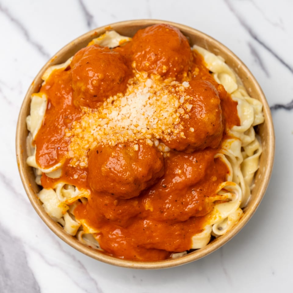 Pasta with meatballs and red sauce, topped with grated cheese in a brown bowl.