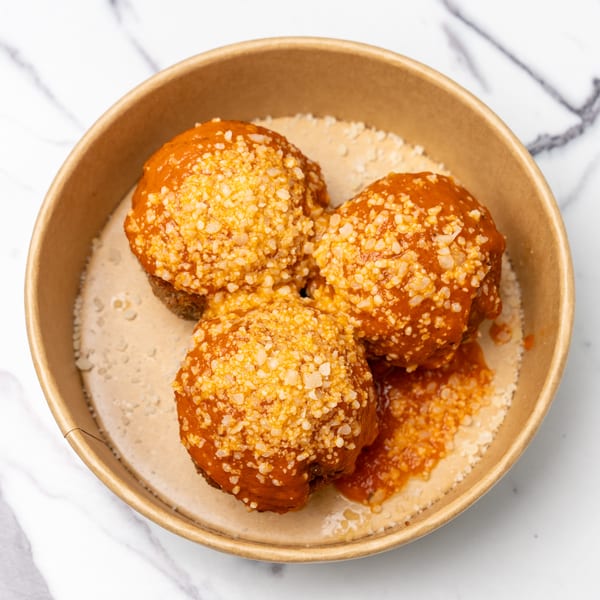 Three meatballs covered in red sauce and grated cheese, served in a brown bowl.