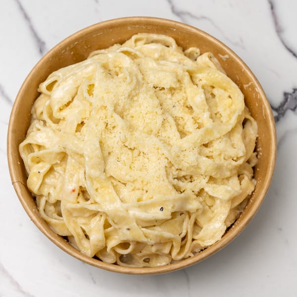 Creamy fettuccine alfredo pasta topped with grated parmesan cheese in a brown bowl.