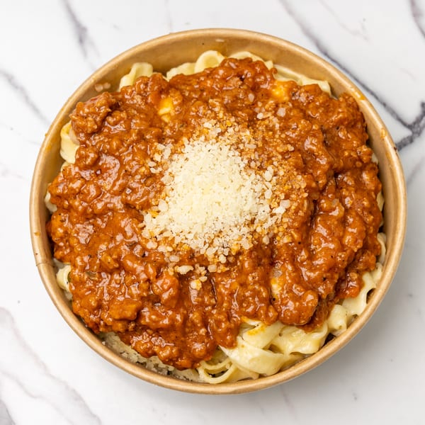 Pasta with a rich red meat sauce and a sprinkle of grated cheese in a round bowl.