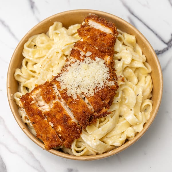 Crispy breaded chicken cutlets with grated cheese on a bed of creamy fettuccine pasta in a bowl.